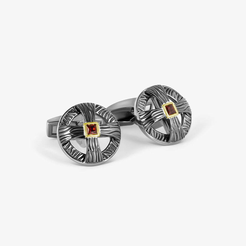 A pair of oxidised sterling silver cufflinks with red and silver colors and yellow gold plating on the garnet centers.