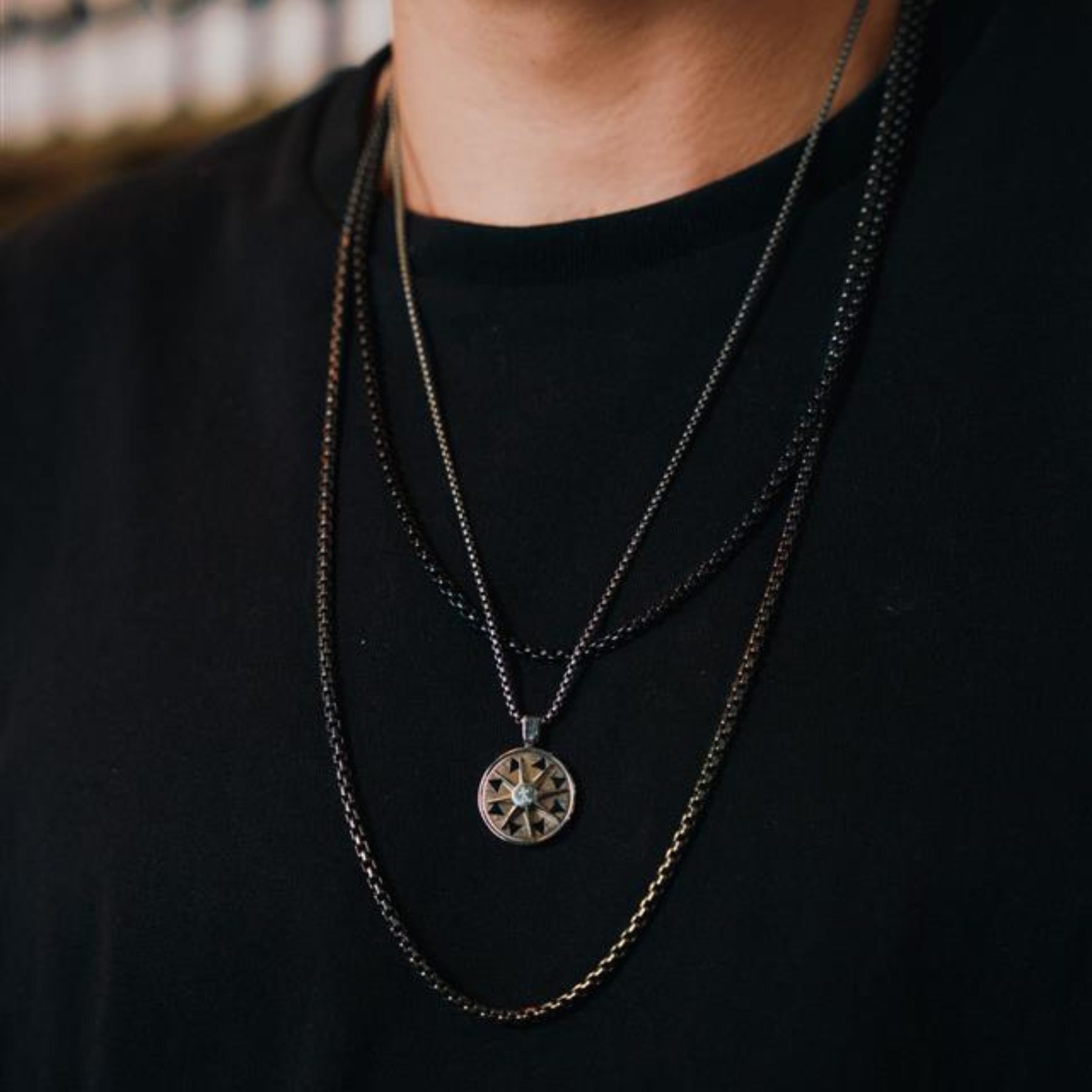 A stainless steel rotating compass amulet necklace with engraved symbols, attached to a silver chain.